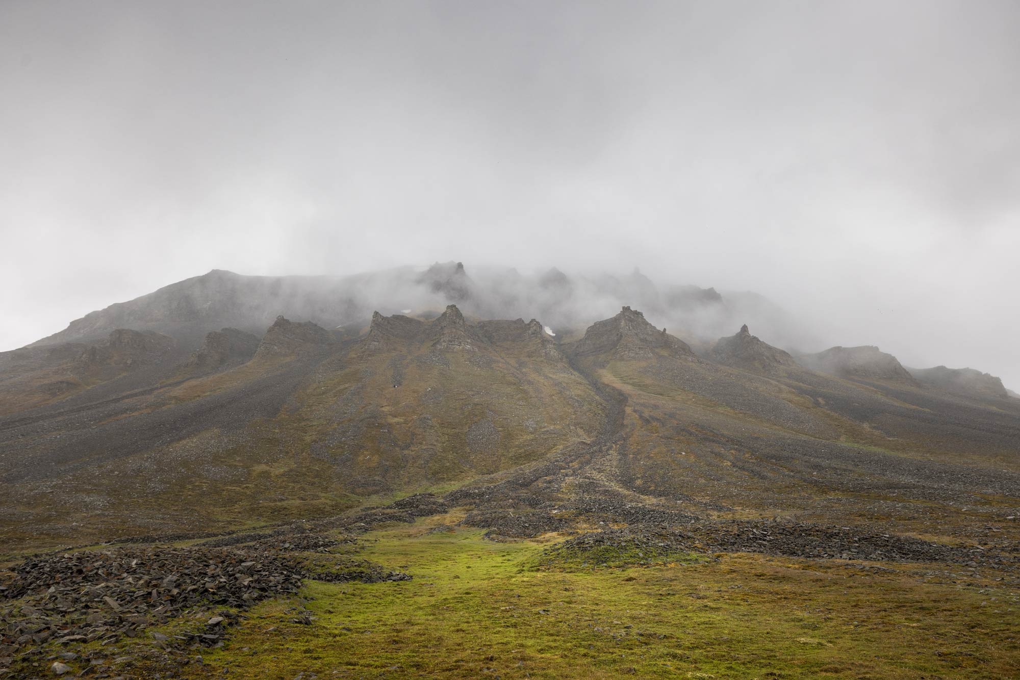 A grassy and rocky ridge, with a higher ridge just beyond it obscured by fog.